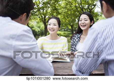 Stock Image - university students working together sitting at wooden out door table . Fotosearch