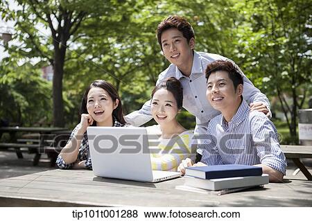 Stock Photo - university students working together with a laptop at wooden out door table . Fotosearch