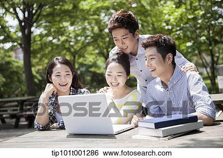 Stock Photograph - university students working together with a laptop at wooden out door table . Fotosearch