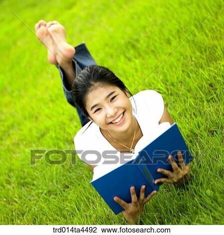 Stock Image - a woman reading a book on the grass. Fotosearch