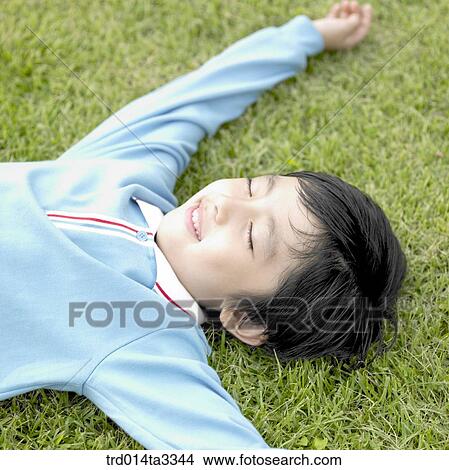 Picture - Boy lying down in the lawn. Fotosearch