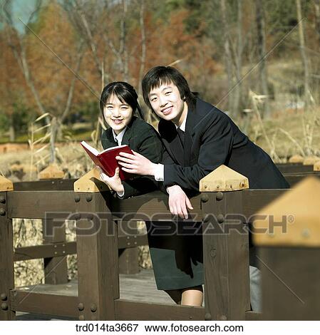 Teens holding books and leanning against fence View Large Photo Image Stock Photo - Teens holding books and leanning against fence. Fotosearch
