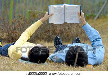 Stock Image - Teens reading books with lying down on the lawn. Fotosearch