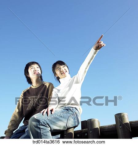 Teens with smile pointing at sky on siitng on the fence View Large Photo Image Stock Photograph - Teens with smile pointing at sky on siitng on the fence. Fotosearch