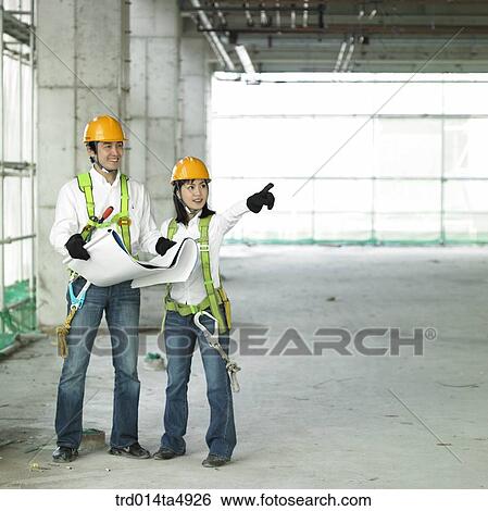 Stock Photograph - at a construction place, an architect looking at a plan and looking around a workplace. Fotosearch