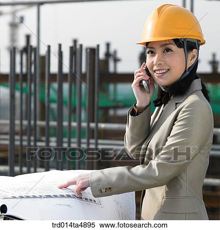 Stock Photography - at a construction place, an architect looking at a plan and talking on the phone. Fotosearch