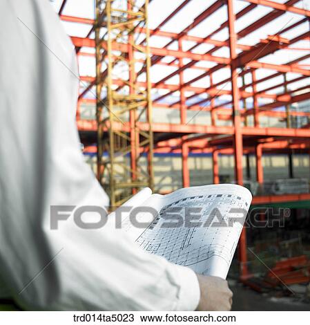 Stock Image - at a construction place, an architect looking at a plan. Fotosearch
