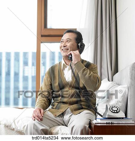 Picture - a calling old man on a bed. Fotosearch