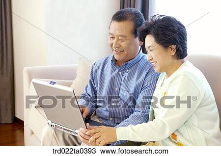 Stock Image - an old couple using a notebook on a sofa. Fotosearch