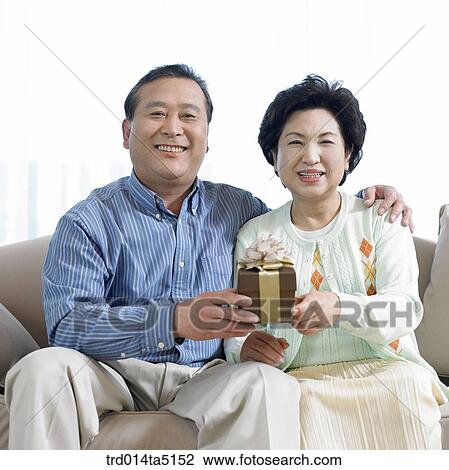 Stock Image - an old couple with a present box on a sofa. Fotosearch