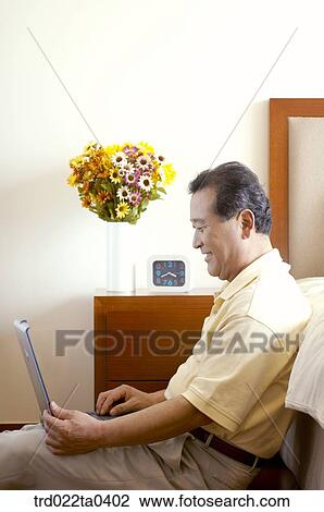 Stock Image - an old man using a notebook on a bed. Fotosearch