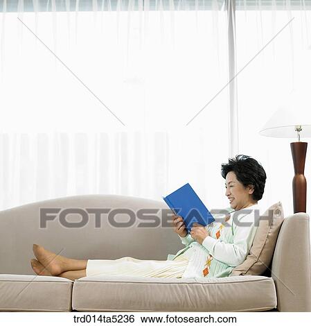 Stock Photograph - an old woman reading a book on a sofa. Fotosearch