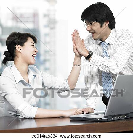 Picture - a businessman and a businesswoman slapping high-fives. Fotosearch