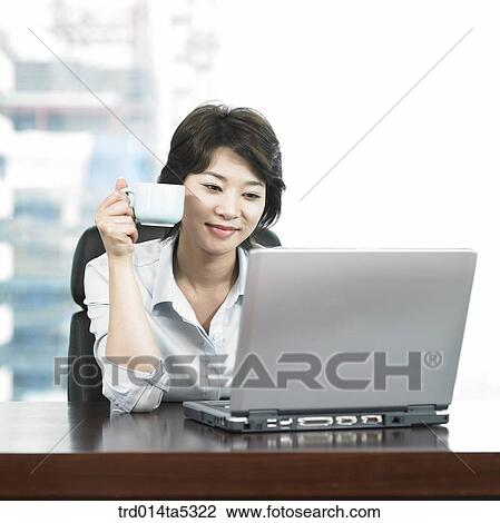 Stock Image - a businessman drinking a tea and looking at a notebook. Fotosearch