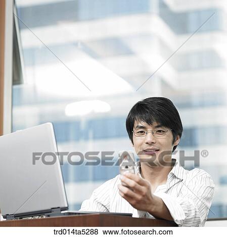 a businessman looking at a mobile phone at a office View Large Photo Image Stock Photo - a businessman looking at a mobile phone at a office. Fotosearch