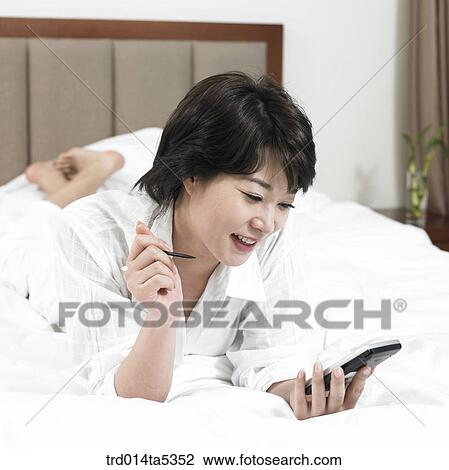 Stock Image - a woman looking at a PDA on a bed. Fotosearch