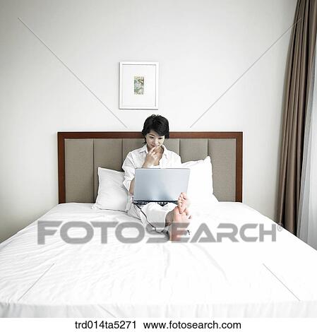 a woman working with a notebook on a bed View Large Photo Image Stock Image - a woman working with a notebook on a bed. Fotosearch