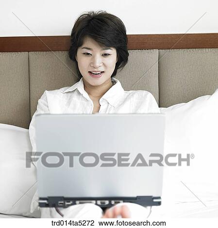 Stock Image - a woman working with a notebook on a bed. Fotosearch