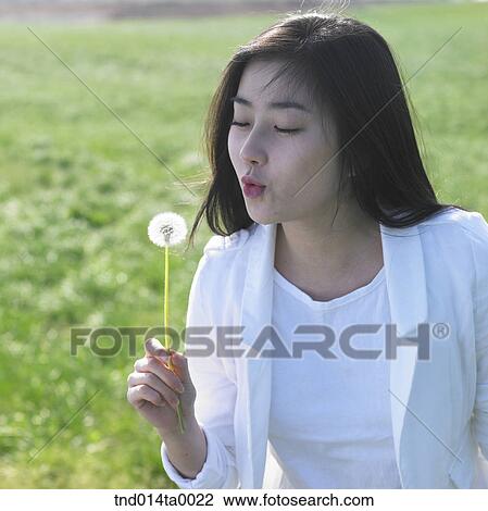 Stock Image - a woman blowing dandelion spores. Fotosearch