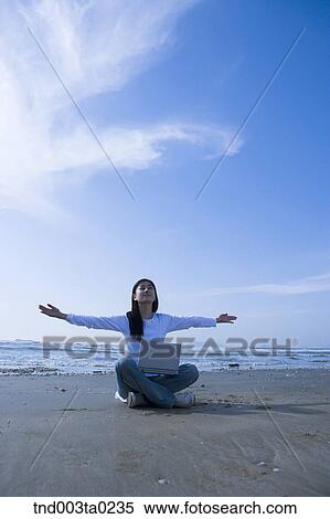 Stock Photography - a woman doing something with a notebook in a sandy beach. Fotosearch