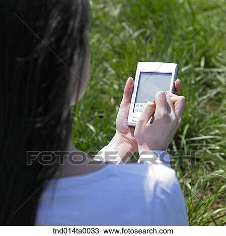 Stock Image - a woman doing something with a PDA on the grass. Fotosearch