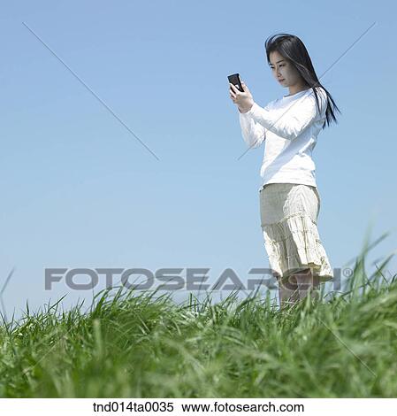 a woman doing something with a PDA on the grass View Large Photo Image Stock Photography - a woman doing something with a PDA on the grass. Fotosearch