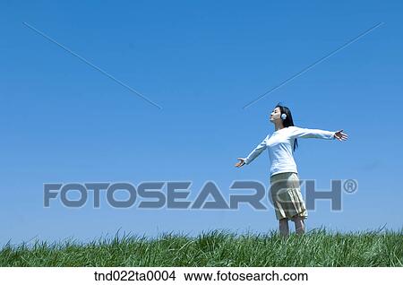 Picture - a woman listening to music with a headset on the grass. Fotosearch