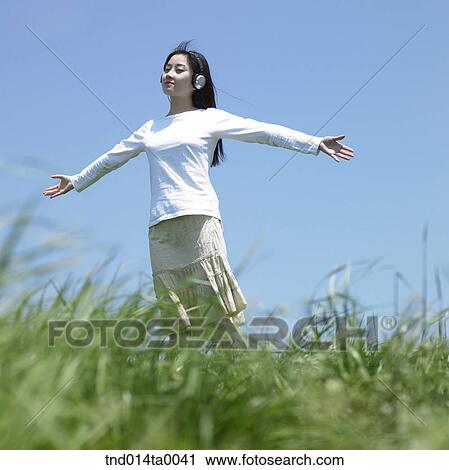 Stock Image - a woman listening to music with a headset on the grass. Fotosearch