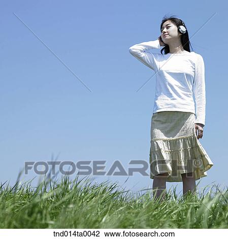 Stock Image - a woman listening to music with a headset on the grass. Fotosearch