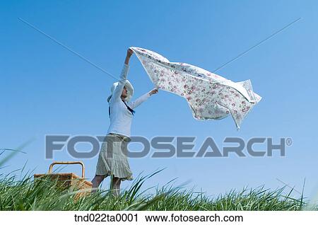 Stock Image - a woman unfolding a mat in the grass. Fotosearch