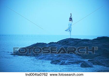 Stock Image - a woman doing Yoga on the rock in a seashore. Fotosearch