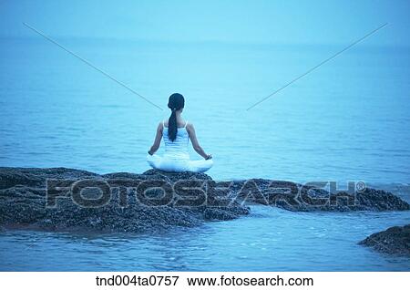 Stock Photo - a woman doing Yoga on the rock in a seashore. Fotosearch