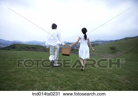 Stock Image - back figure of the couple with picnic bag on the field. Fotosearch