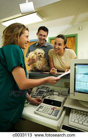 A Vet Tech Shows A Couple Paperwork At The Front Desk Of The Vet