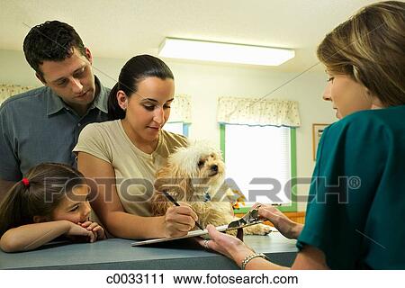 A Woman Signs Paperwork At The Desk Of The Vet Clinic While