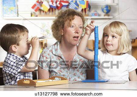 Stock Photo - Adult Helping Two Young Children at Montessori/Pre-School. Fotosearch