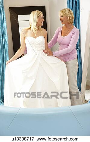 Stock Photo - Bride trying on wedding dress with sales assistant. Fotosearch