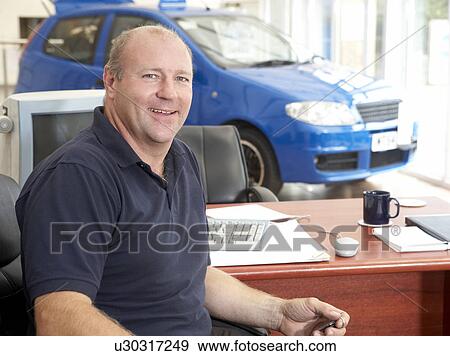 Stock Photo - Car salesman sitting in showroom smiling. Fotosearch