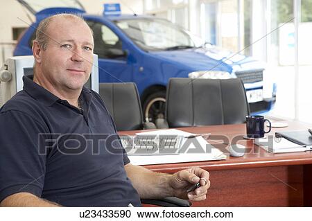 Stock Image - Car salesman sitting in showroom. Fotosearch