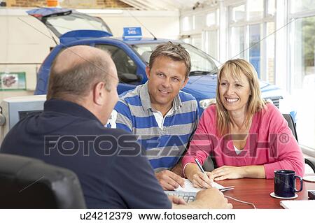 Stock Photo - Couple filling in paperwork in car showroom. Fotosearch