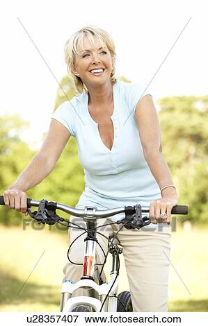 Stock Photo - Portrait of mature woman riding cycle in countryside. Fotosearch