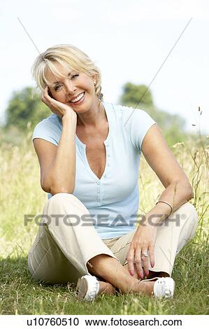 Stock Image - Portrait of mature woman sitting in countryside. Fotosearch