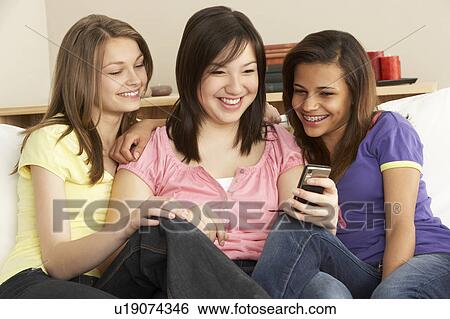 Teenage Girlfriends Reading Mobile Phone at Home View Large Photo Image Stock Photograph - Teenage Girlfriends Reading Mobile Phone at Home. Fotosearch