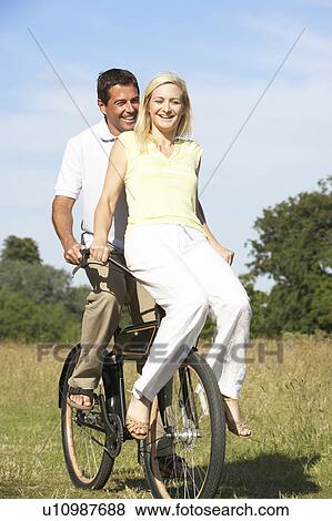 Stock Photo - Young couple riding bike in countryside. Fotosearch