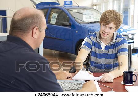 Young man filling in paperwork in car showroom View Large Photo Image Picture - Young man filling in paperwork in car showroom. Fotosearch