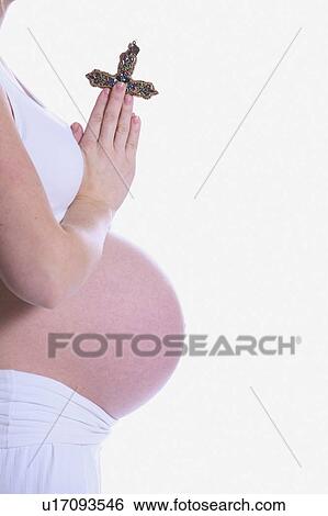 Stock Photograph - Pregnant woman praying with a cross in her hands. Fotosearch
