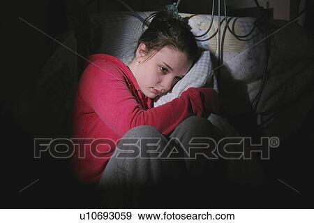 Stock Photo - Scared teenage girl sitting in bedroom. Fotosearch