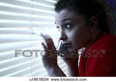 Picture - Teenage girl on the phone, peeking out the window. Fotosearch