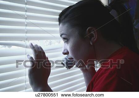 Stock Image - Teenage girl on the phone, peeking out a window. Fotosearch
