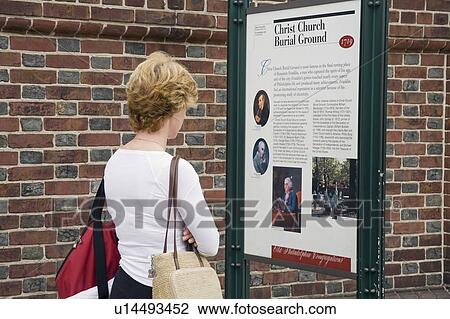 Stock Image - Woman reading park information sign. Fotosearch